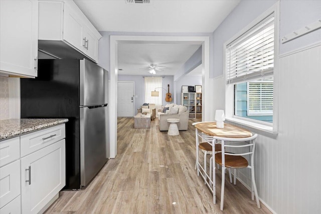 kitchen with light wood-type flooring, freestanding refrigerator, a ceiling fan, and white cabinetry