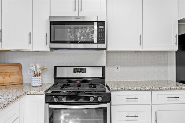 kitchen featuring tasteful backsplash, white cabinets, appliances with stainless steel finishes, and light stone countertops