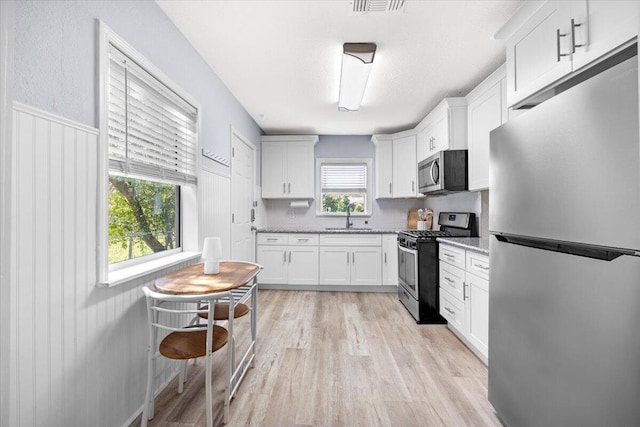 kitchen featuring a sink, light wood finished floors, white cabinetry, and stainless steel appliances