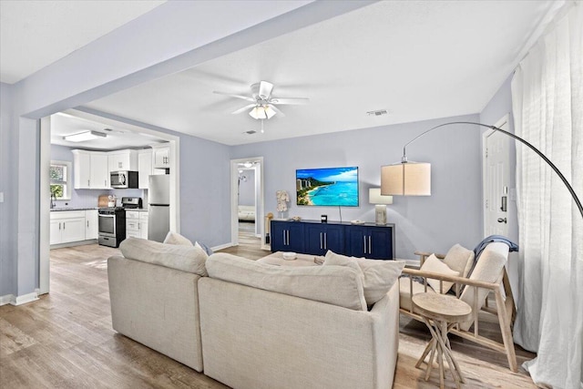 living area featuring visible vents, light wood-style floors, baseboards, and ceiling fan