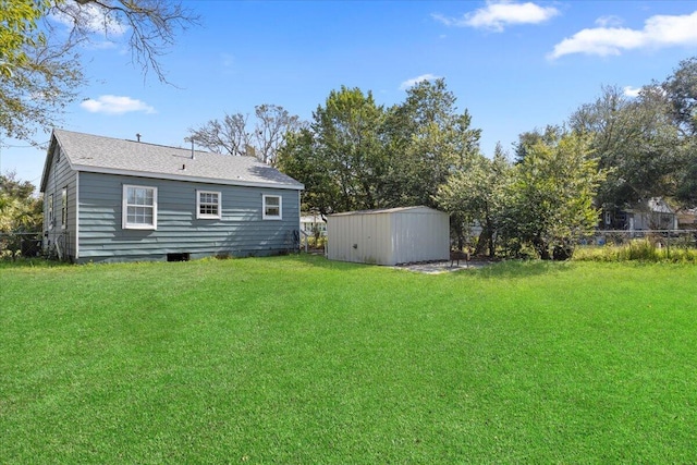 back of house featuring a shingled roof, fence, a lawn, an outdoor structure, and a storage unit