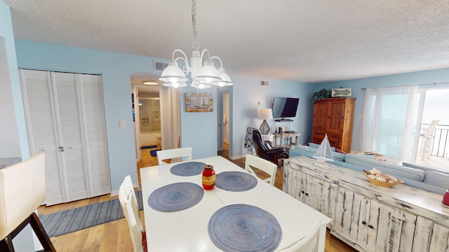 dining room with visible vents, a textured ceiling, light wood finished floors, and an inviting chandelier