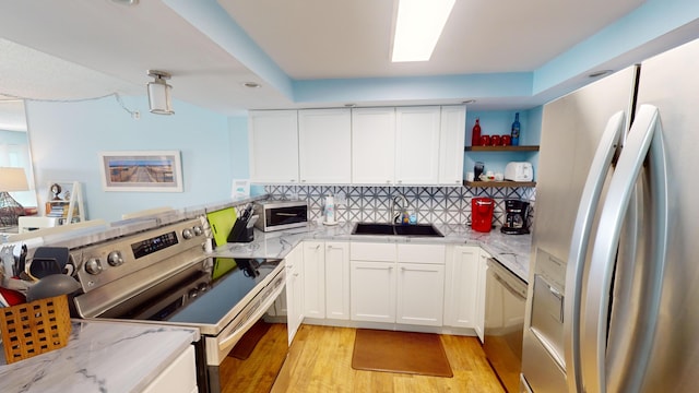 kitchen with open shelves, appliances with stainless steel finishes, a sink, and light stone countertops