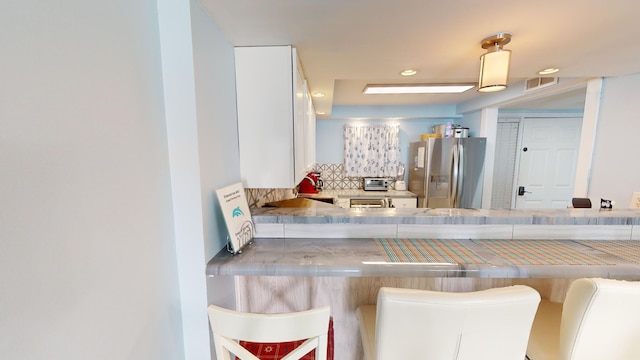 kitchen with tasteful backsplash, a breakfast bar area, visible vents, and stainless steel fridge with ice dispenser