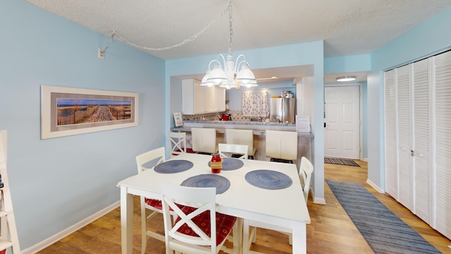 dining area featuring light wood finished floors, a textured ceiling, baseboards, and a notable chandelier