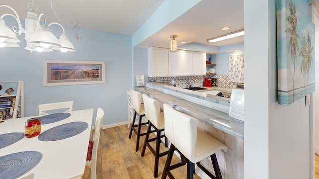 kitchen featuring white cabinetry, light countertops, light wood finished floors, a kitchen bar, and tasteful backsplash