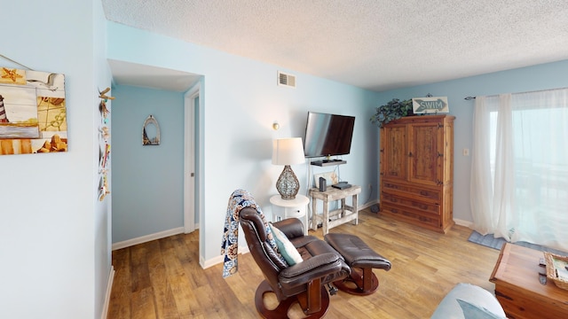 living area featuring light wood-style floors, baseboards, visible vents, and a textured ceiling