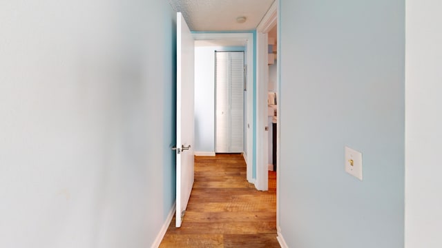 hall with a textured ceiling, baseboards, and wood finished floors