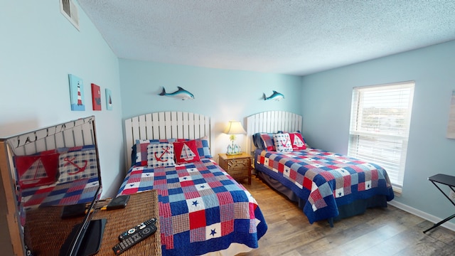 bedroom featuring a textured ceiling, wood finished floors, visible vents, and baseboards