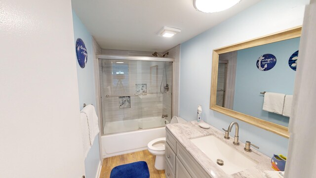 bathroom featuring shower / bath combination with glass door, vanity, toilet, and wood finished floors