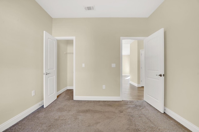 unfurnished bedroom featuring carpet, a spacious closet, visible vents, and baseboards