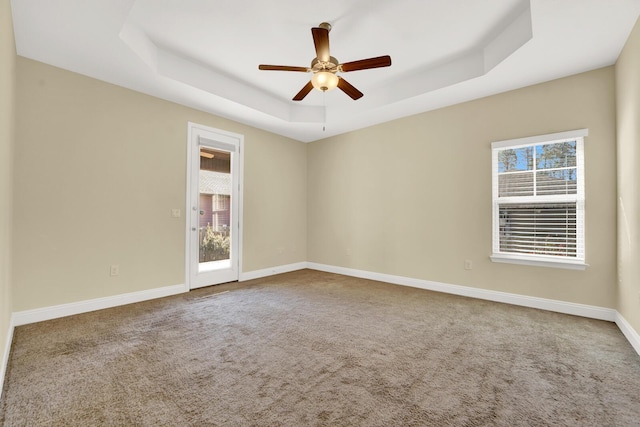 carpeted empty room with a healthy amount of sunlight, baseboards, a raised ceiling, and a ceiling fan