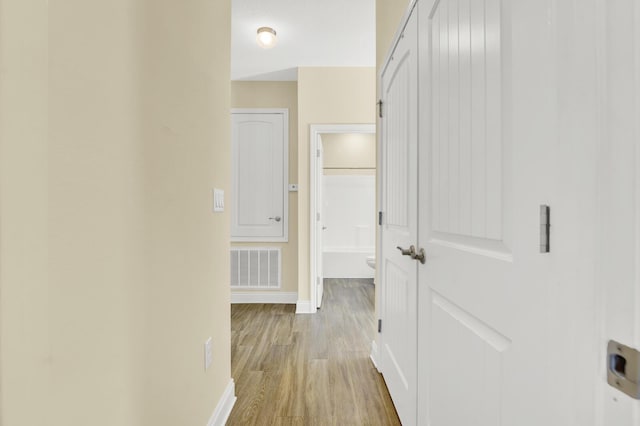 corridor with light wood finished floors, visible vents, and baseboards