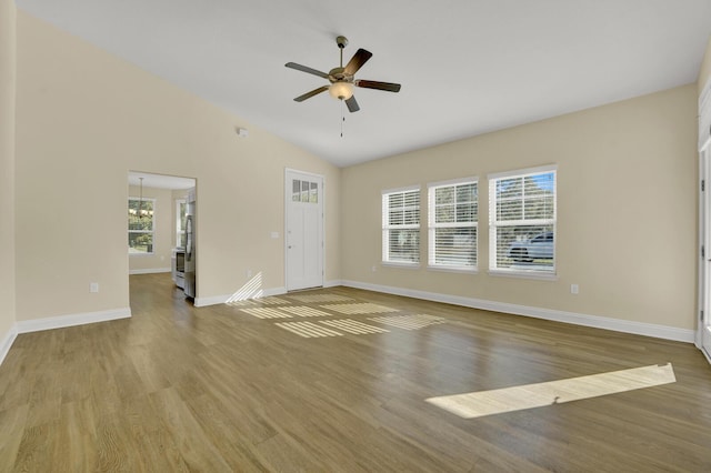 unfurnished living room featuring vaulted ceiling, ceiling fan with notable chandelier, wood finished floors, and baseboards