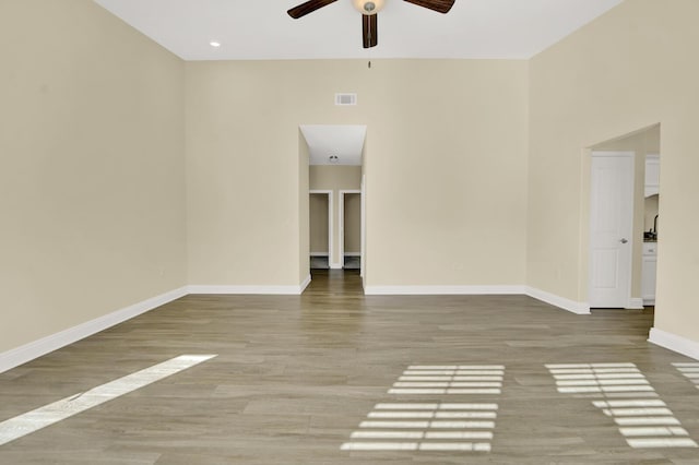 unfurnished room with ceiling fan, wood finished floors, visible vents, and baseboards