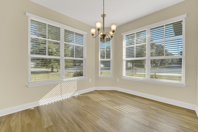 unfurnished dining area with an inviting chandelier, baseboards, and wood finished floors