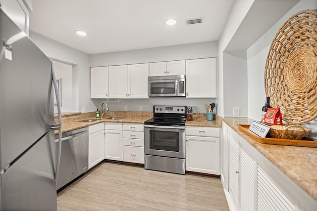 kitchen with light wood finished floors, visible vents, appliances with stainless steel finishes, white cabinetry, and a sink