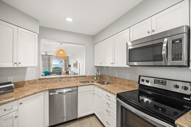 kitchen with light wood finished floors, stainless steel appliances, white cabinets, a sink, and light stone countertops