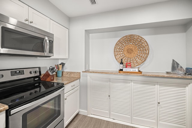 kitchen featuring stainless steel appliances, white cabinetry, visible vents, and light wood finished floors