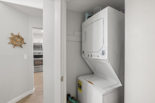 laundry area with light wood-style flooring, stacked washer and clothes dryer, and baseboards