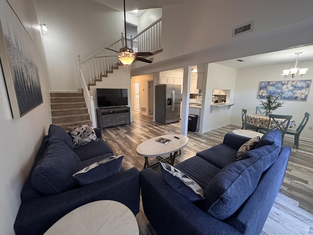 living room with visible vents, wood finished floors, a towering ceiling, stairway, and a chandelier