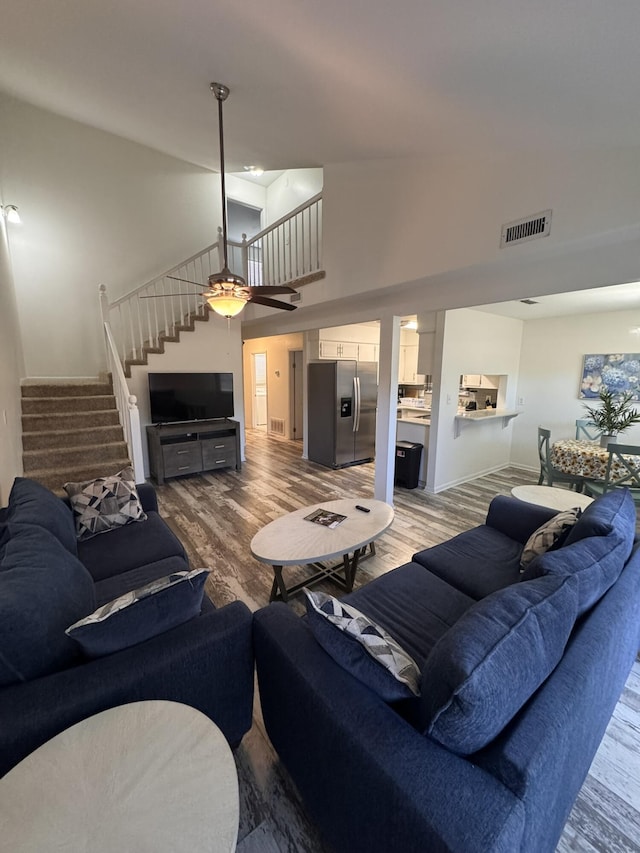 living area featuring visible vents, high vaulted ceiling, wood finished floors, stairway, and baseboards