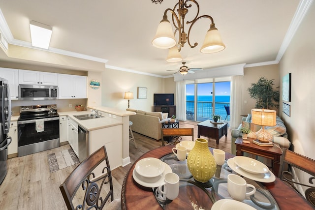 kitchen featuring light wood-style flooring, appliances with stainless steel finishes, open floor plan, crown molding, and a sink