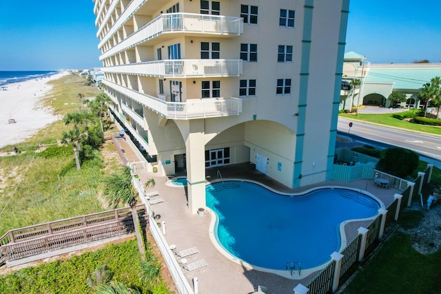 view of swimming pool with a water view, fence, a beach view, and a patio