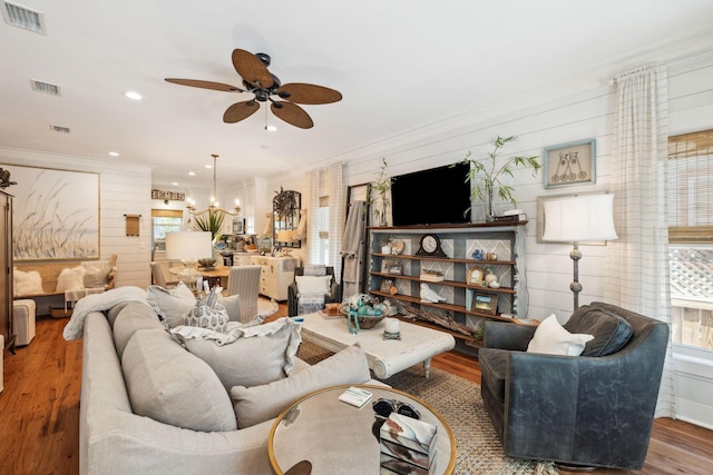 living room with visible vents, ornamental molding, ceiling fan with notable chandelier, and wood finished floors