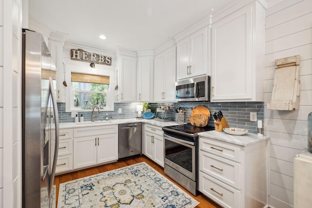 kitchen with a sink, tasteful backsplash, wood finished floors, white cabinetry, and appliances with stainless steel finishes