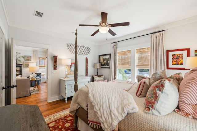 bedroom with a ceiling fan, wood finished floors, visible vents, baseboards, and crown molding