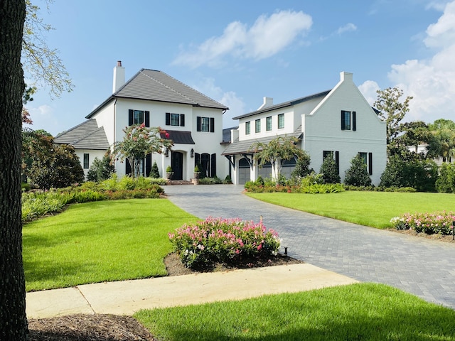 view of front of property with decorative driveway, a chimney, and a front lawn