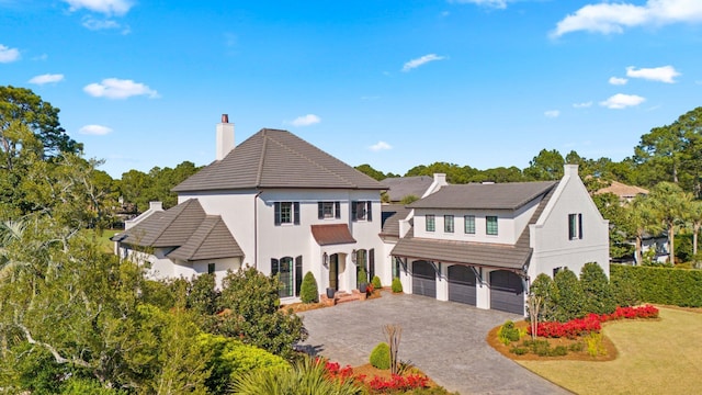 view of front facade featuring stucco siding, a chimney, an attached garage, decorative driveway, and a front yard