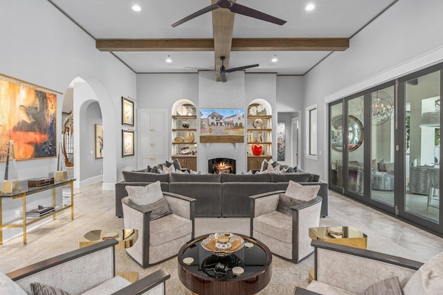 living room with a large fireplace, ceiling fan, beamed ceiling, and arched walkways