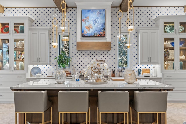 kitchen featuring light stone counters, an island with sink, glass insert cabinets, and wallpapered walls