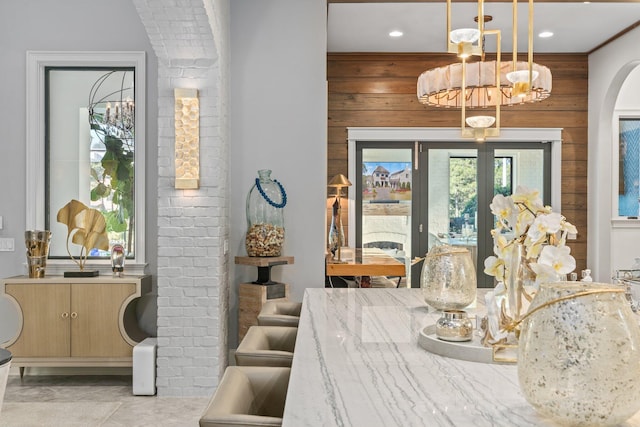 dining space with arched walkways, french doors, wood walls, and an inviting chandelier