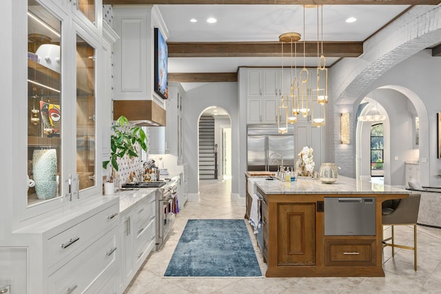 kitchen with light stone counters, arched walkways, a notable chandelier, high end appliances, and white cabinetry