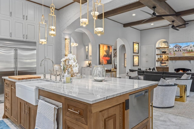 kitchen with beam ceiling, open floor plan, stainless steel built in fridge, a large fireplace, and a sink