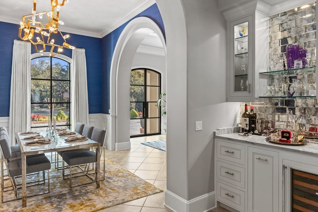 bar with an inviting chandelier, light tile patterned floors, arched walkways, and crown molding