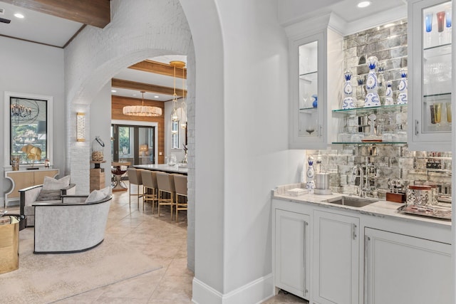 bar with arched walkways, indoor wet bar, beamed ceiling, a sink, and backsplash