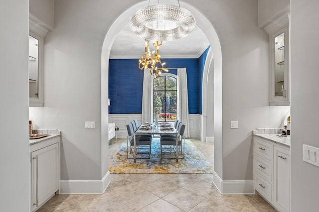 dining space with a wainscoted wall, a chandelier, arched walkways, and a decorative wall