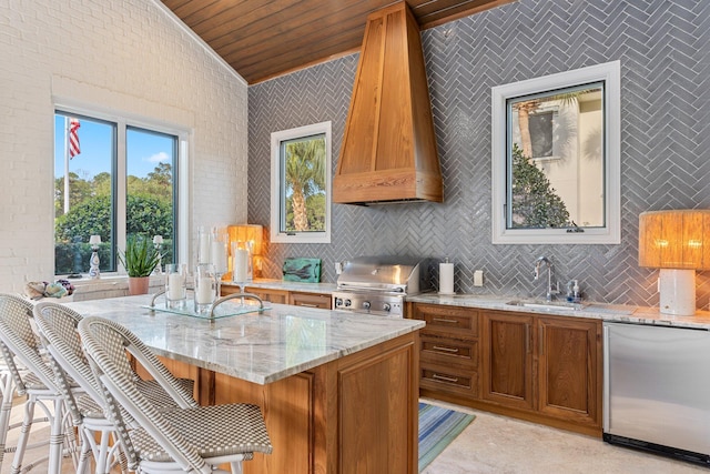 kitchen with light stone counters, a sink, fridge, custom exhaust hood, and brown cabinetry