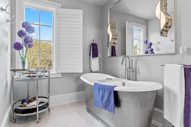 bathroom with marble finish floor, a soaking tub, a wealth of natural light, and baseboards