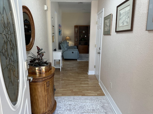 corridor featuring baseboards, light wood-style floors, and a textured wall