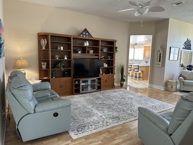 living area with visible vents, a textured ceiling, light wood finished floors, ceiling fan, and a textured wall