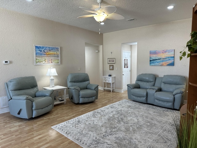 living area featuring visible vents, a textured ceiling, light wood finished floors, ceiling fan, and a textured wall