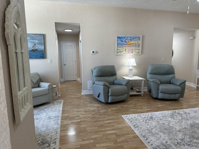 living area with wood finished floors, visible vents, a textured wall, and baseboards