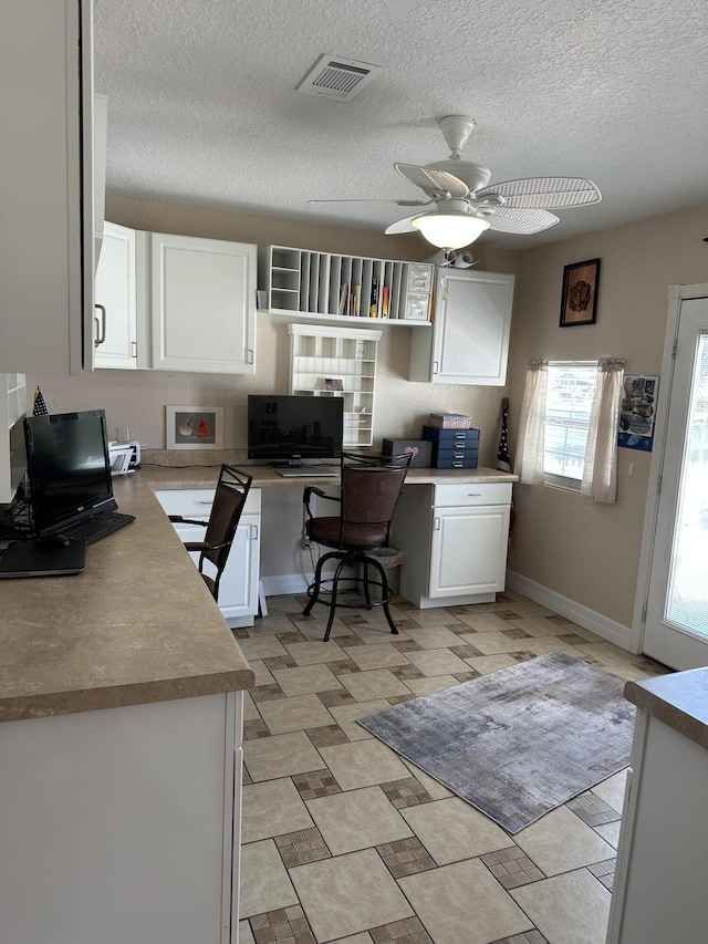 office area featuring visible vents, a textured ceiling, baseboards, ceiling fan, and built in study area