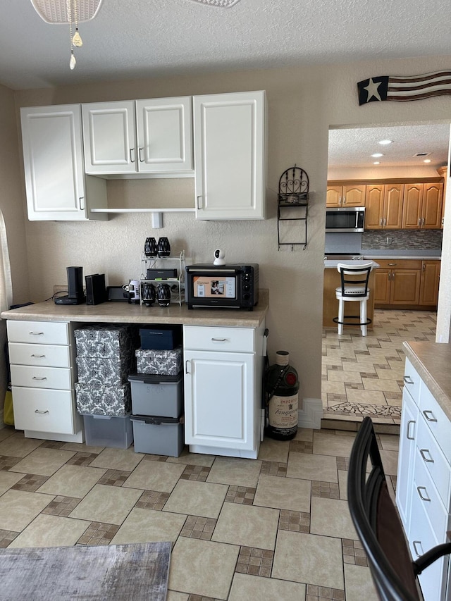 kitchen featuring stainless steel microwave, white cabinetry, light countertops, and decorative backsplash