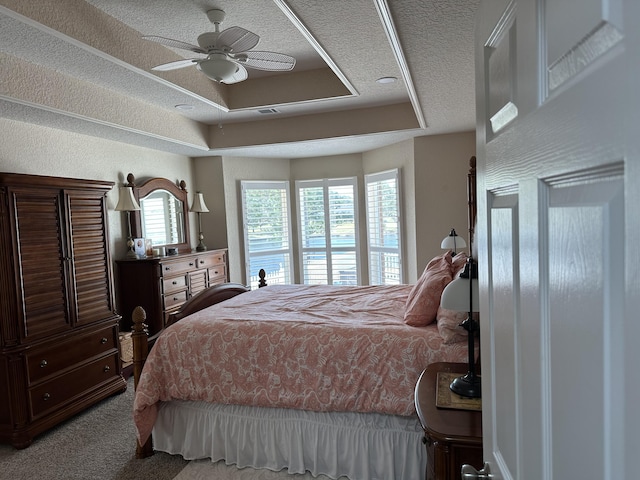 bedroom with carpet flooring, a textured ceiling, a raised ceiling, and a ceiling fan